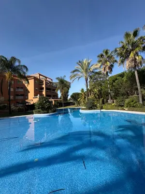 a large blue swimming pool with palm trees in the background at Áncora apartamento in El Puerto de Santa María