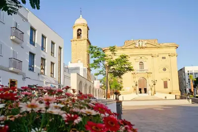 a building with a clock tower and flowers in front of it at Cozy Apart. Costa Sancti Petri by Chiclana Dreams in Novo Sancti Petri