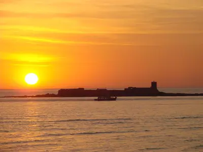a sunset over a body of water with a lighthouse at Apartamento Costa de Sancti Petri by Chiclana Dreams in Novo Sancti Petri