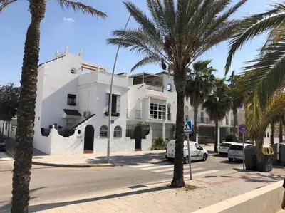 a white building with palm trees in front of it at Dúplex 4, primera línea de Playa in Sanlúcar de Barrameda