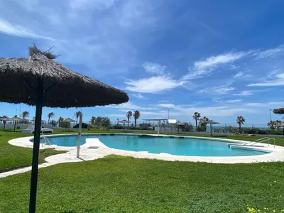 a large swimming pool with an umbrella and grass at Modern Beach Front Home by Chiclana Dreams in Chiclana de la Frontera