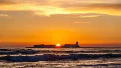 a sunset over the ocean with a lighthouse in the distance at Piso Centro Chiclana in Chiclana de la Frontera