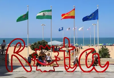 a sign on the beach with many flags at Apartamento patio Andaluz in Rota
