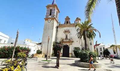 a woman walking in front of a building with a clock tower at YourHouse Apartamentos Andasol 1 I in Chipiona