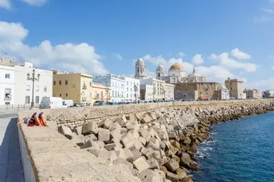 a group of people sitting on a wall next to the water at Apartamento PUERTA-CALETA by Cadiz4Rentals in Cádiz