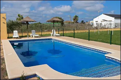 a large swimming pool with two chairs and a fence at Bungalow en complejo II in Conil de la Frontera