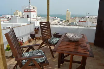 a wooden table and chairs on a balcony with a lighthouse at Apartamento El Mirador de Cadiz in Cádiz