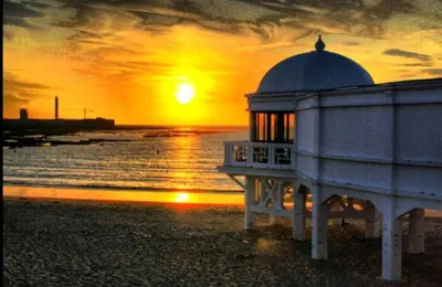 a building on the beach with a sunset in the background at Casa Caleta a 2 minutos de la playa in Cádiz