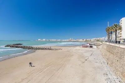 a person standing on a beach next to the ocean at Apartamento La Pepa de ORO by Cadiz4Rentals in Cádiz