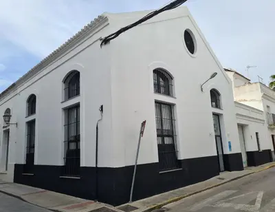 a white building with black windows on a street at Bodega Mar - Solera in Sanlúcar de Barrameda