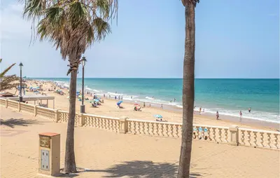 a beach with palm trees and people on the beach at 6 Bedroom Gorgeous Home In Chipiona in Chipiona