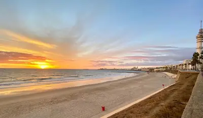 a beach with a lighthouse and the ocean at sunset at El Destino Corazón de Cádiz Grupo AC Gestion in Cádiz