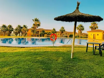 a table with a straw umbrella next to a swimming pool at Mika's House Lite in Sanlúcar de Barrameda